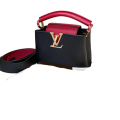 Louis Vuitton Capucines Mini bag in black Taurillon leather with contrasting red top handle. Features gold-tone LV initials clasp and removable strap. Front view.